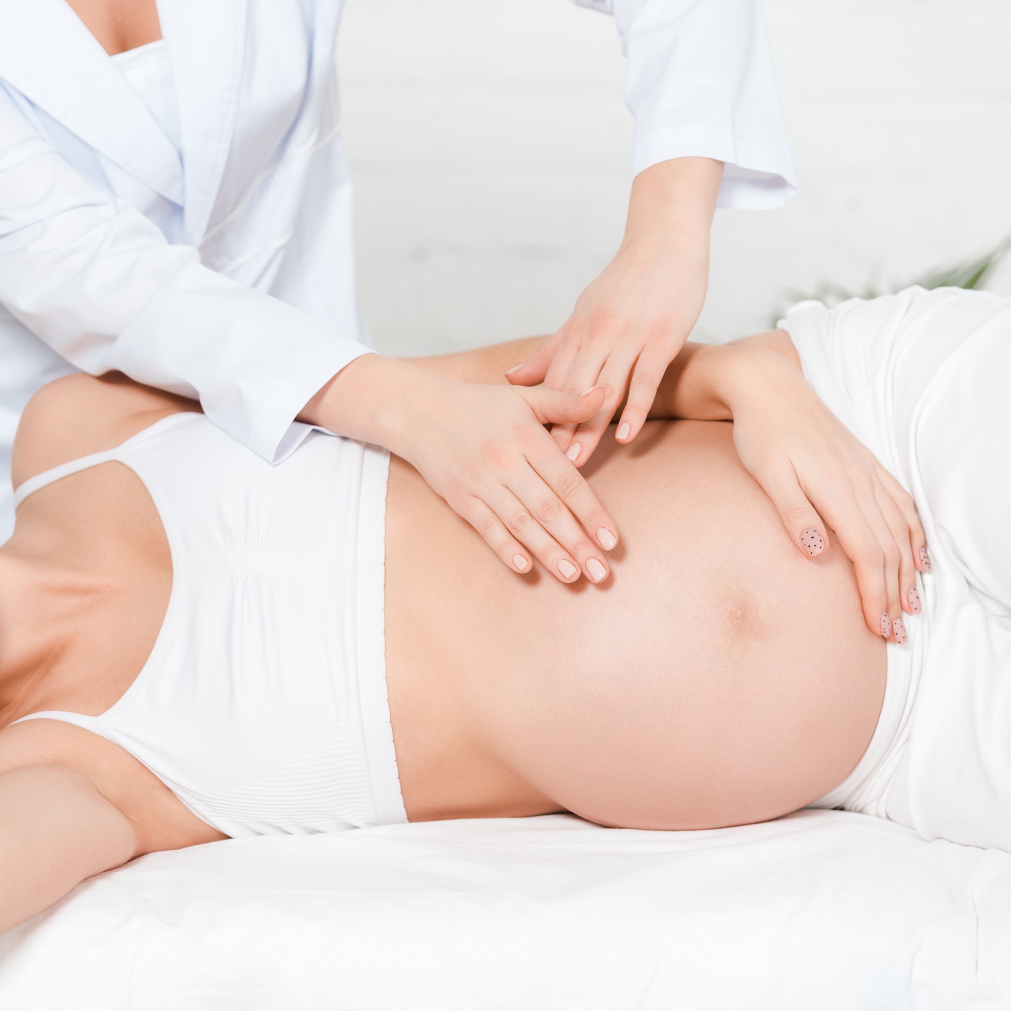 Cropped view of masseur doing belly massage to pregnant woman on massage table